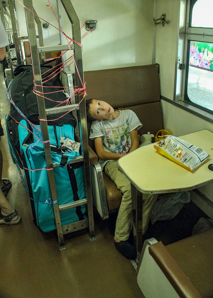 A boy sits in a seat in the night train from Chiang Mai to Bangkok eating chips