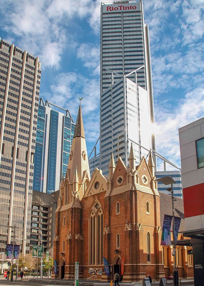 A historic church building stands in front of modern skyscrapers, including one with the Rio Tinto logo