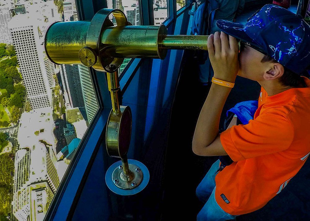 Child looking through a telescope at the Sydney Tower Eye, observing the cityscape from a high vantage point