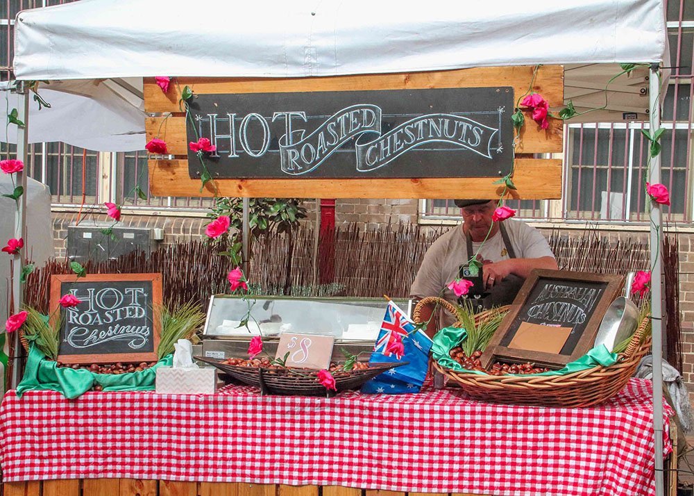 Stall at The Rocks market in Sydney selling hot roasted chestnuts, decorated with chalkboard signs and red gingham tablecloth.