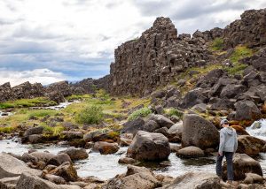 Rocky stream flowing through a rugged landscape surrounded by large boulders and cliffs. A teenage boy is standing on one of the boulders.