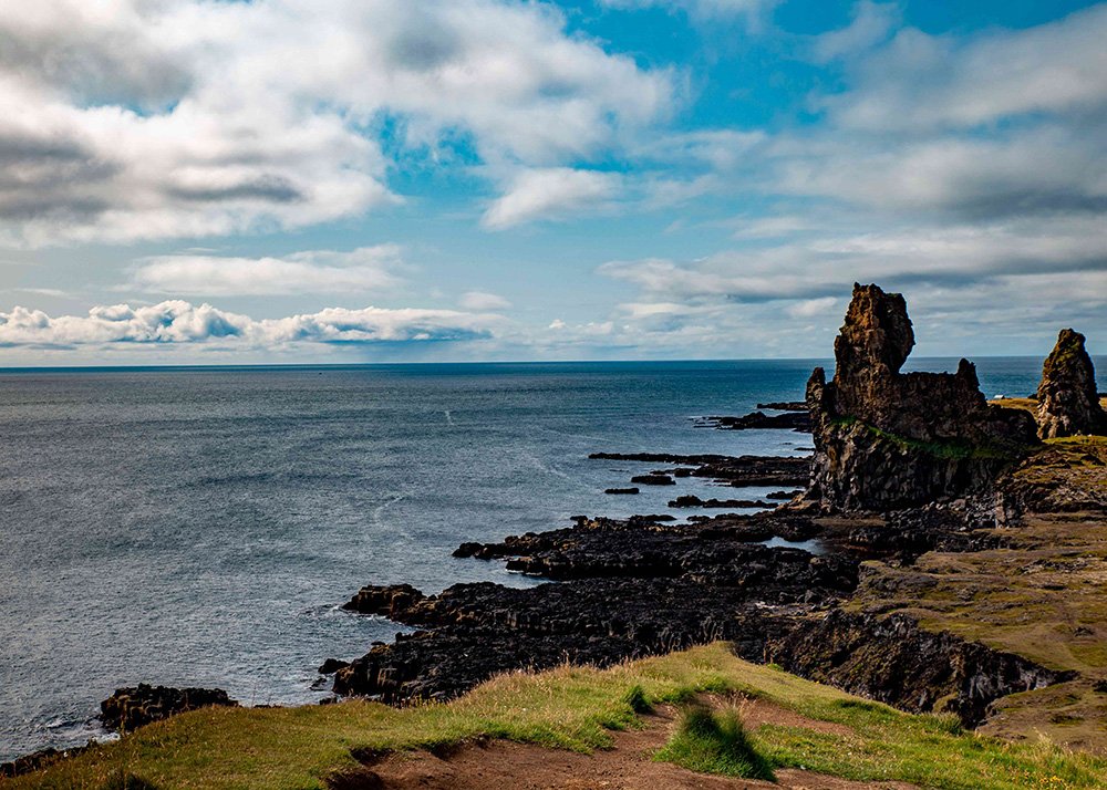 The rugged coastline at Londrangar with dark volcanic rocks jutting out into the ocean, with cloudy skies overhead.