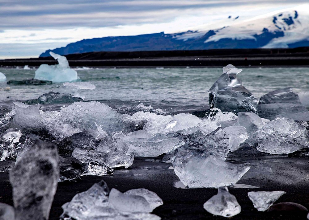 Pieces of ice scattered on the black sand at Diamond Beach with a glacier visible in the background.