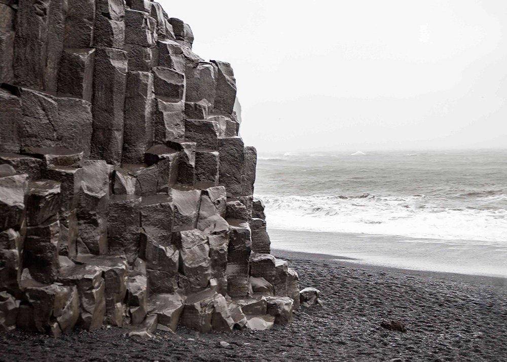 Tall, angular basalt columns on the black sand beach in Reynisfjara with waves crashing in the background.