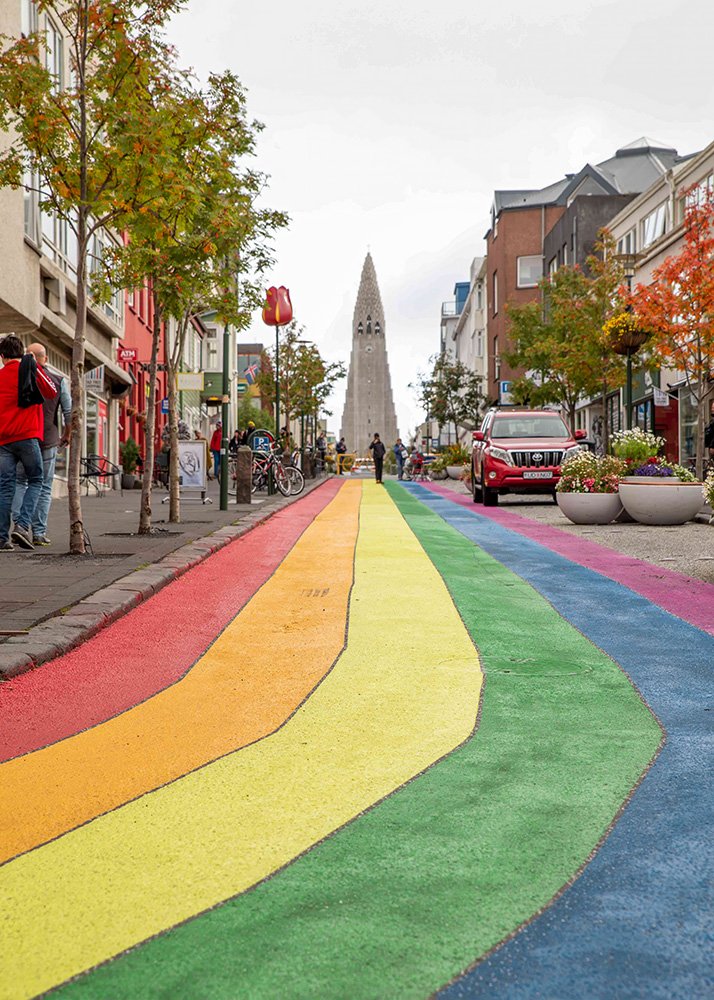 A vibrant rainbow-painted street in Reykjavik, Iceland, with the Hallgrimskirkja church towering in the background.