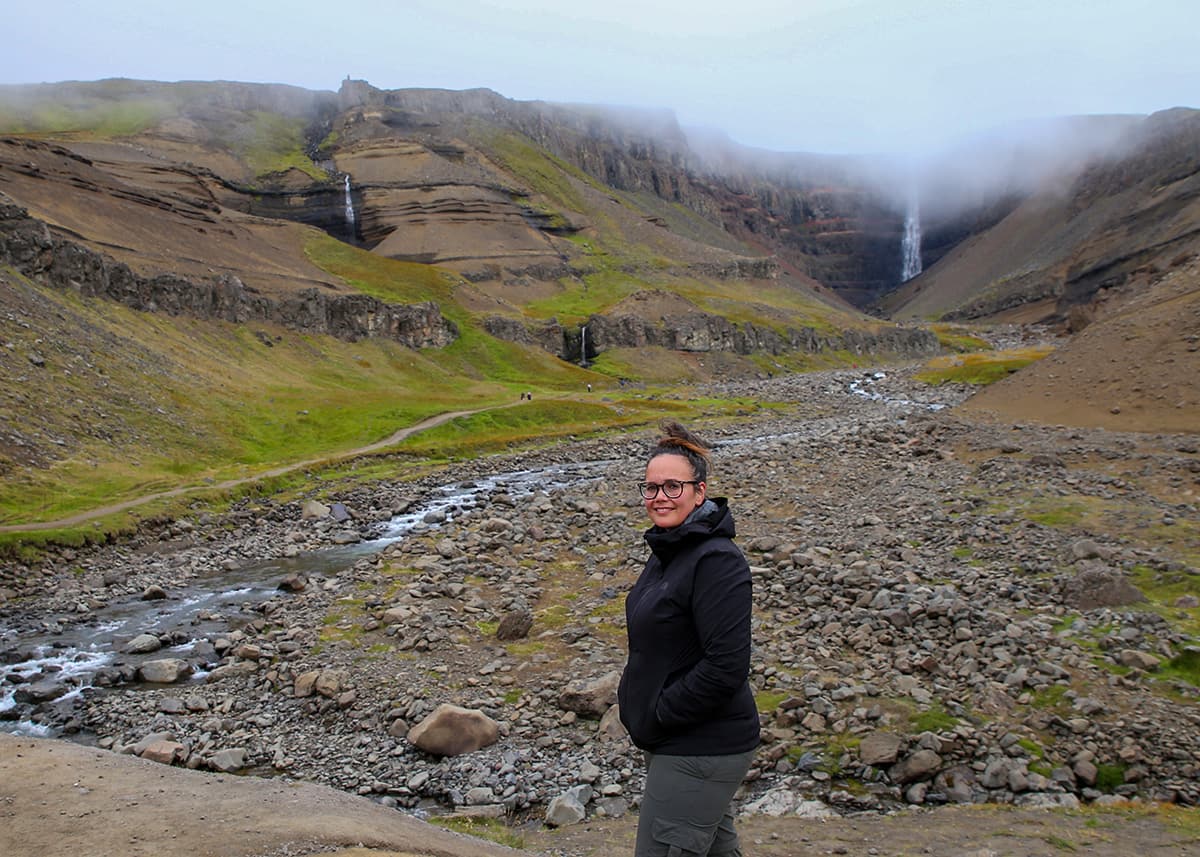 A woman poses in front of waterfall Hengifoss in Iceland.