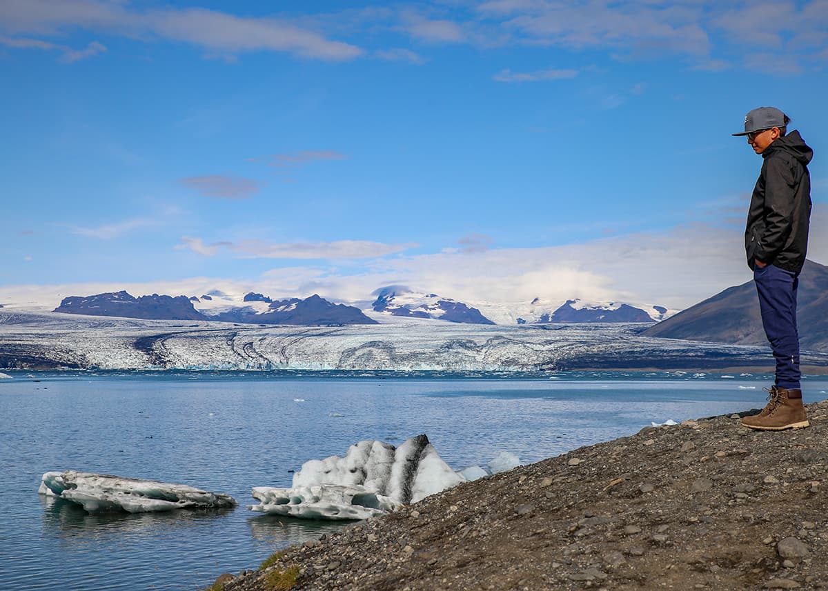 A teen admires the view of Jokulsarlon glacier lake filled with small icebergs and a glacier in the distance.