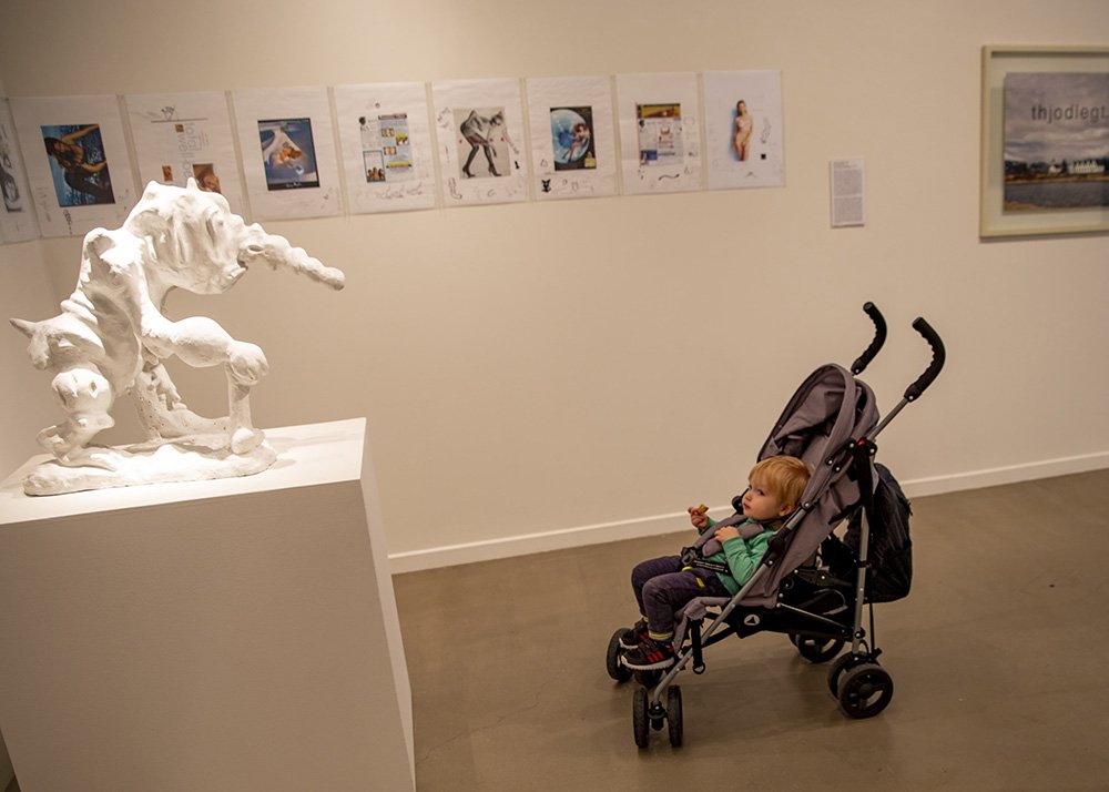 A child in a stroller observing a white sculptural art piece in Reykjavik's National Art Gallery.