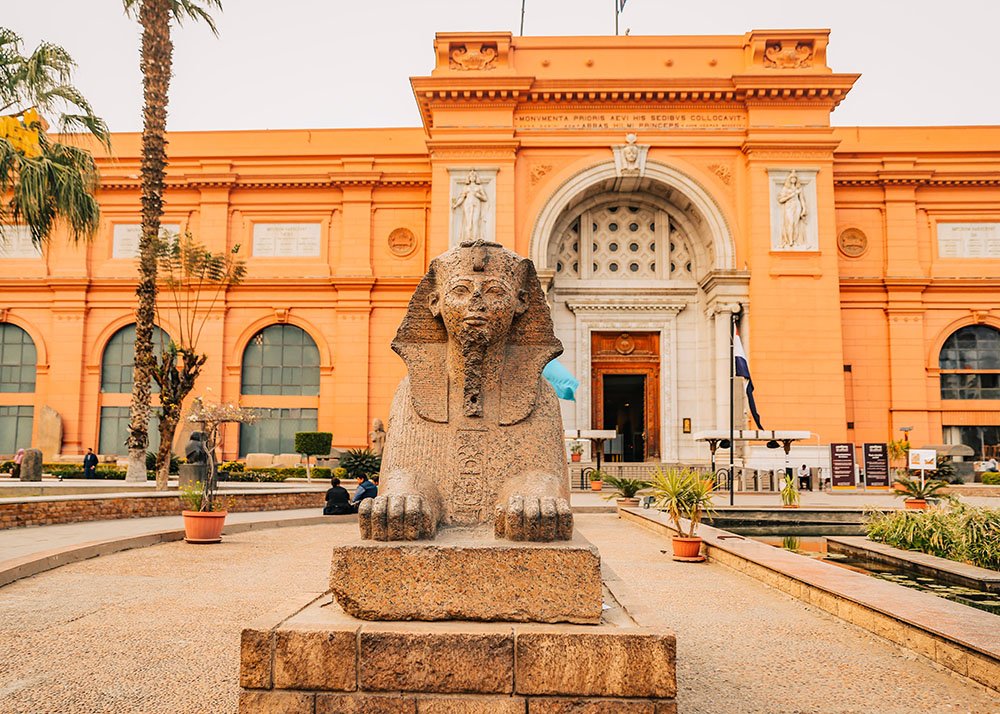 The entrance to the Egyptian Museum in Cairo, featuring a sphinx statue in the foreground and the building's grand facade.