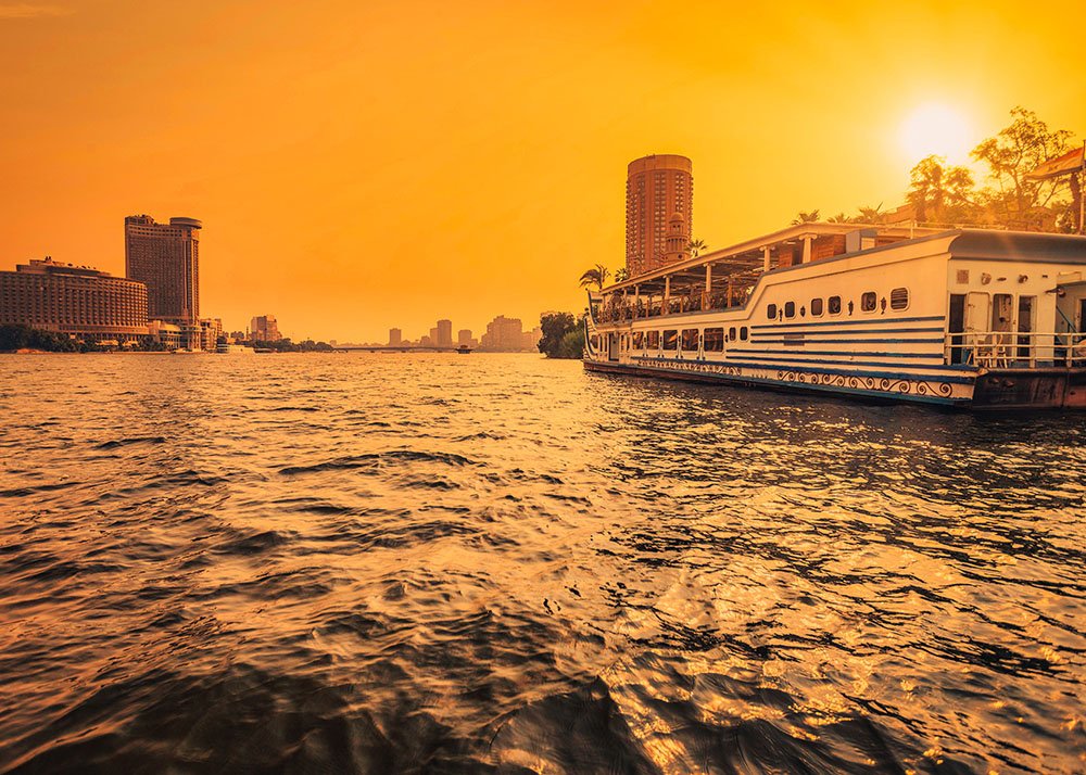 A cruise ship on the Nile River during sunset, with the skyline of Cairo in the background.