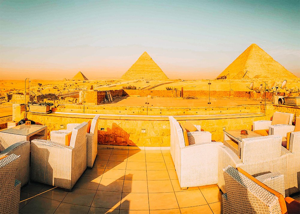 A rooftop terrace with wicker furniture offering a panoramic view of the Pyramids of Giza.