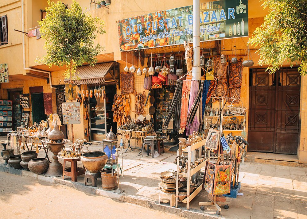 Street view of Old Fustat Bazaar in Cairo, Egypt, showcasing an array of traditional Egyptian gifts and artifacts displayed outside the shop.