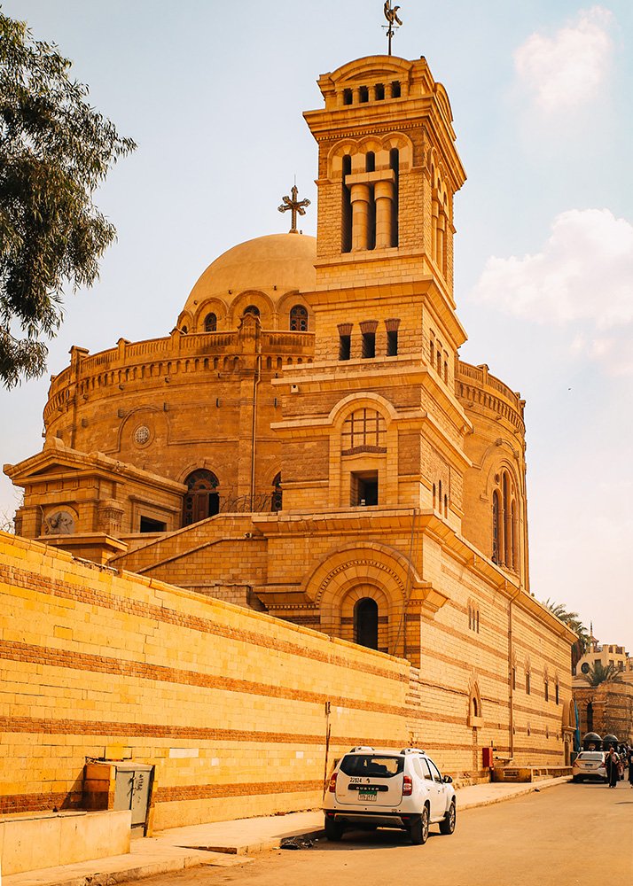 Exterior of the Hanging Church (Saint Virgin Mary's Coptic Orthodox Church) in Cairo, Egypt, with a beige stone façade and a dome.