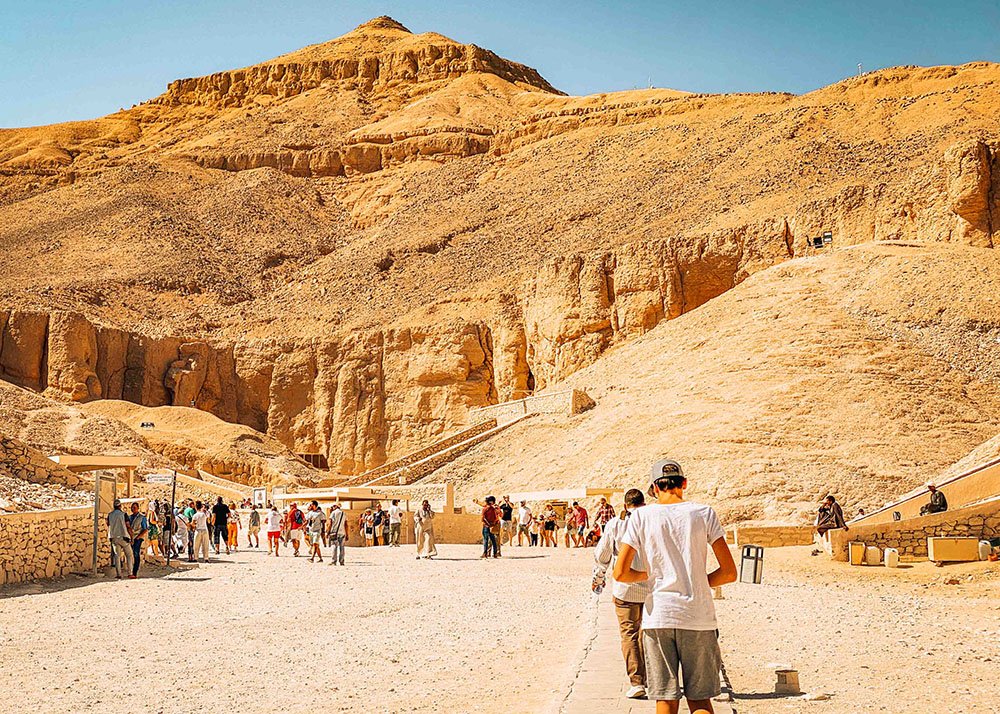 Visitors walking through the Valley of the Kings, with the surrounding arid hills and ancient tombs visible.
