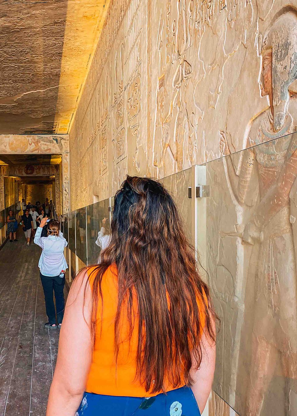 A person walking through a corridor with ancient Egyptian carvings on the walls, inside a tomb in the Valley of the kings