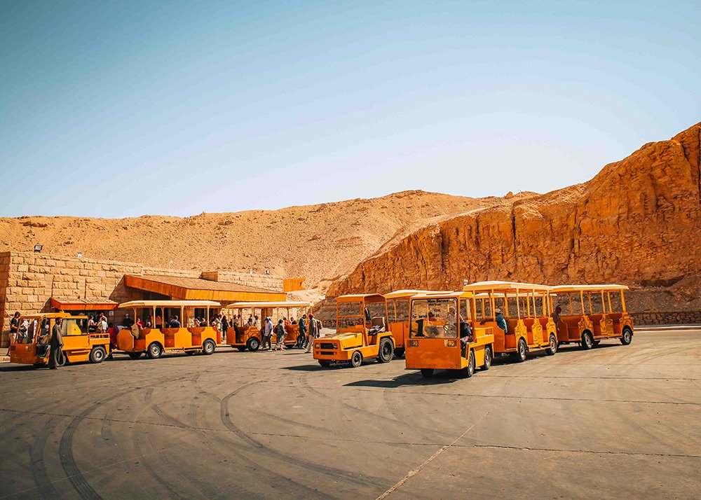 Yellow tourist trams parked in a lot surrounded by rocky hills in the Valley of the Kings.