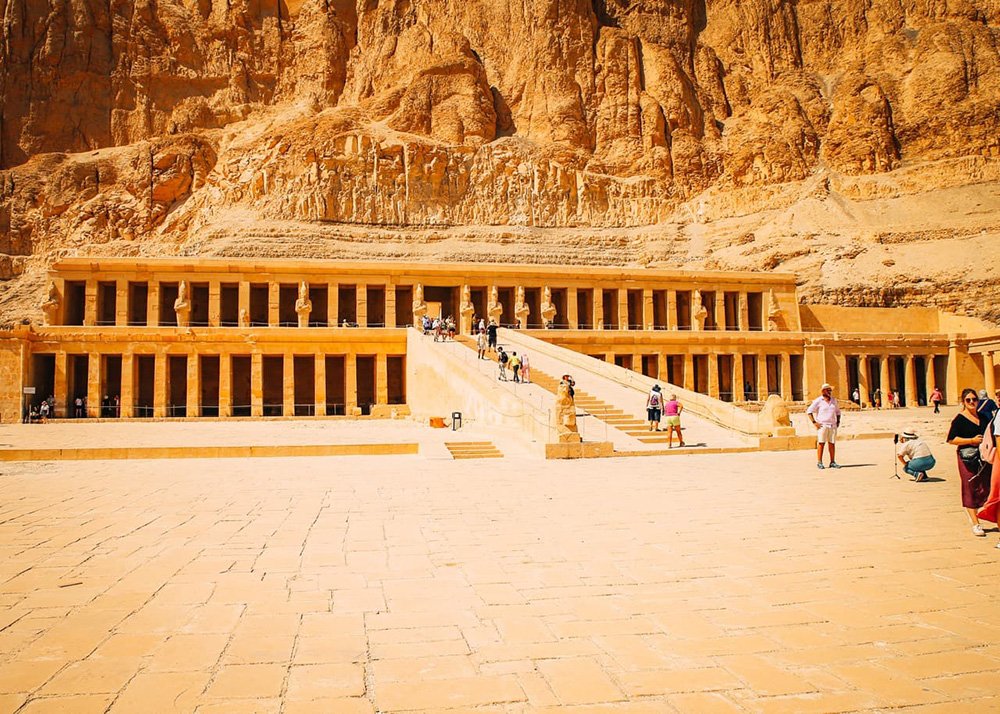 The Temple of Hatshepsut with its grand, tiered structure set against a rocky cliff, with tourists exploring the site
