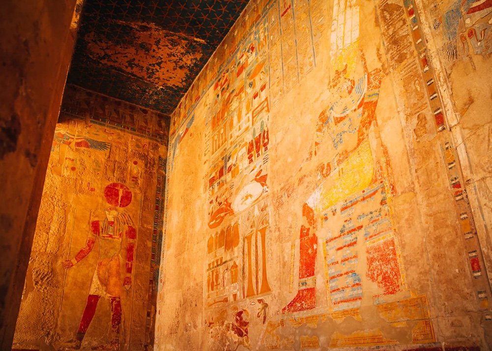 Colorful ancient Egyptian wall paintings with detailed hieroglyphics inside the temple of Hatshepsut, showcasing scenes of daily life and deities.