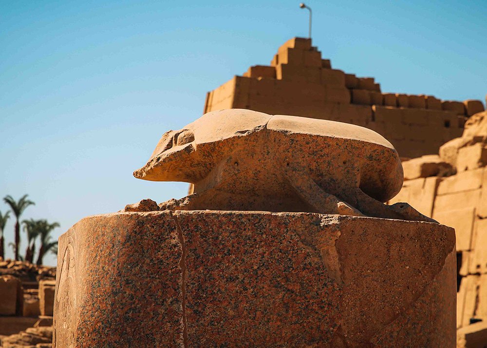 The sacred scarab beetle statue at Karnak Temple, carved from stone and placed on a pedestal.