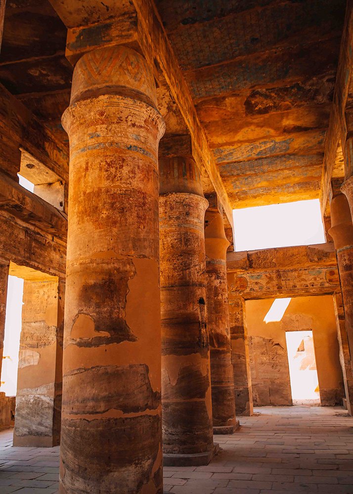 The interior columns of an ancient Egyptian temple in the Karnak complex, with faded paint and hieroglyphics still visible on the pillars.