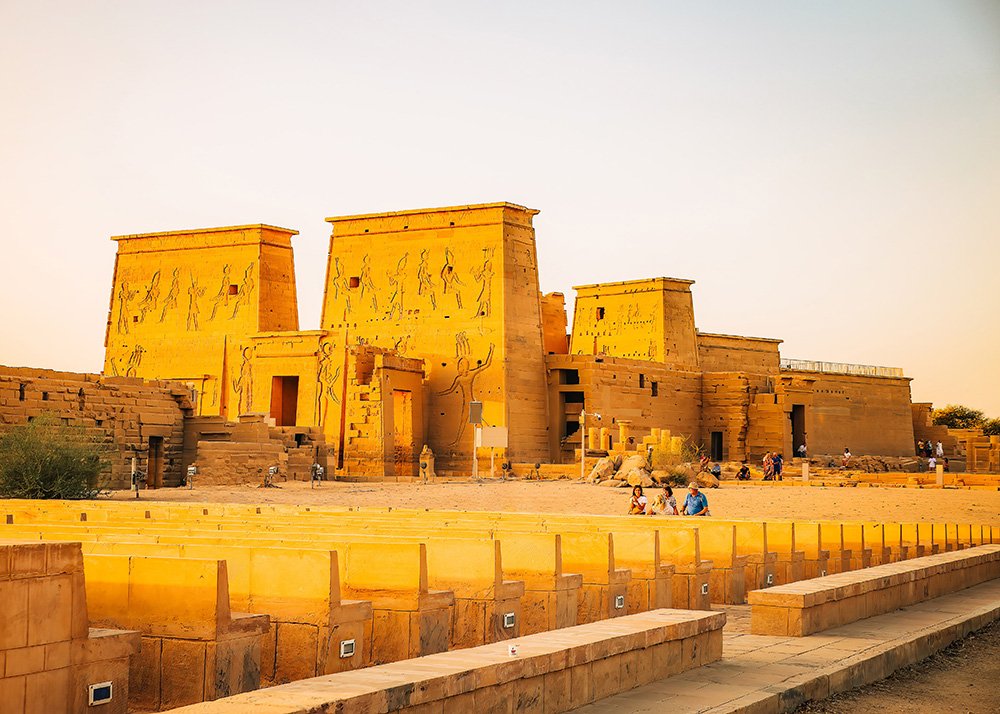 View of the Philae Temple complex at sunset, with its large stone structures and hieroglyphs, against a clear sky.