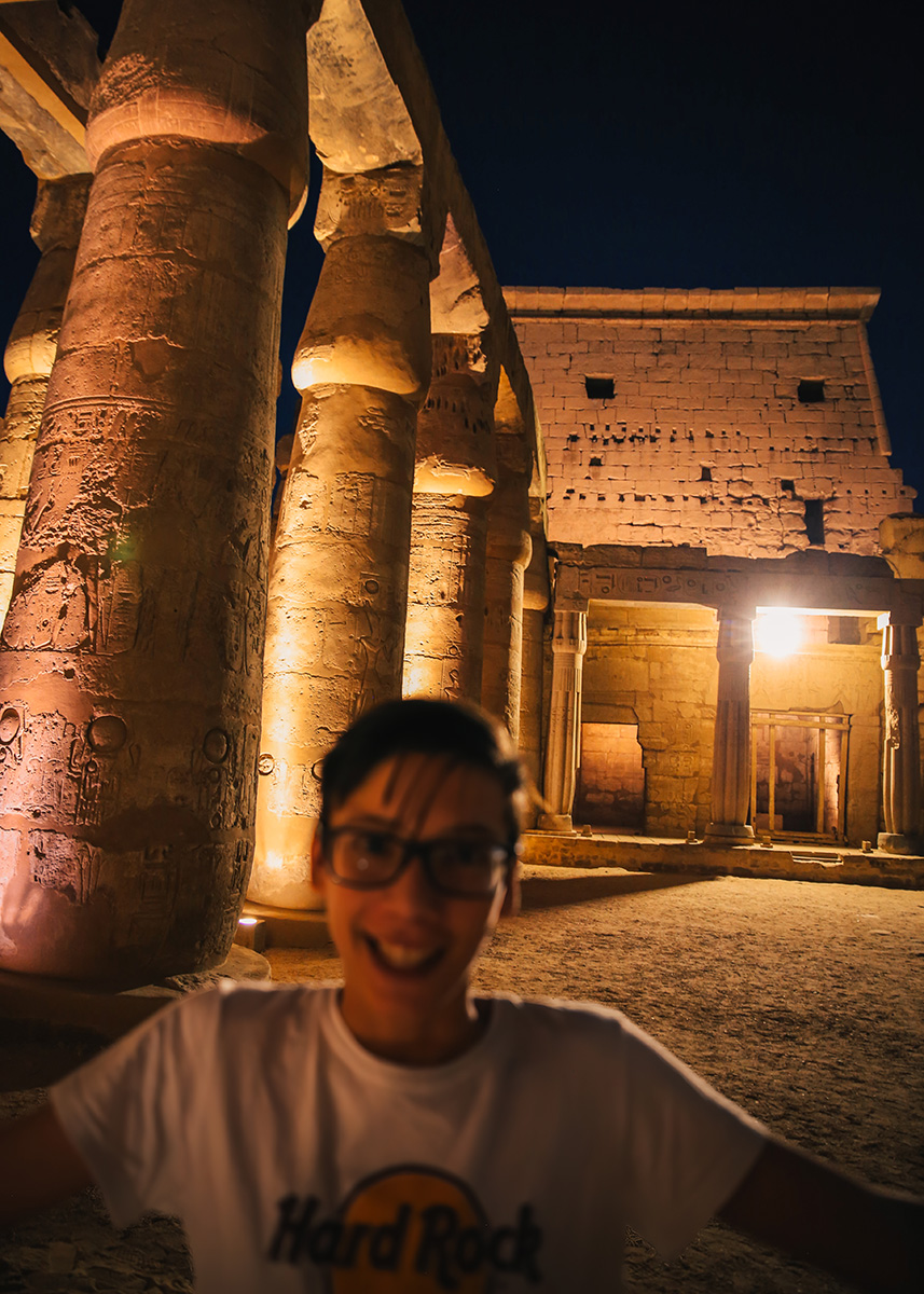 A smiling child stands in front of massive, illuminated hieroglyph-covered columns inside Luxor Temple after dark. The scene captures the temple’s scale and mystery, lit by soft spotlights. Exploring at night adds a sense of magic and adventure for families.