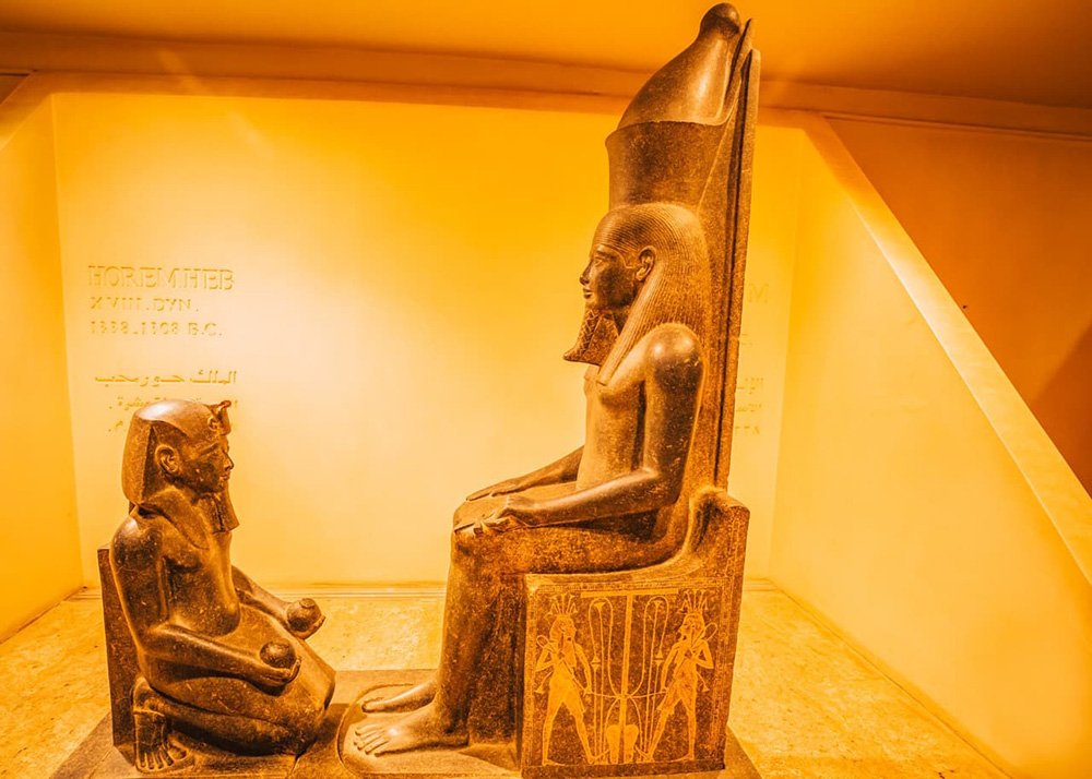 Statue of Pharaoh Horemheb from the 18th Dynasty, depicted seated with another figure kneeling, displayed in Luxor Museum.