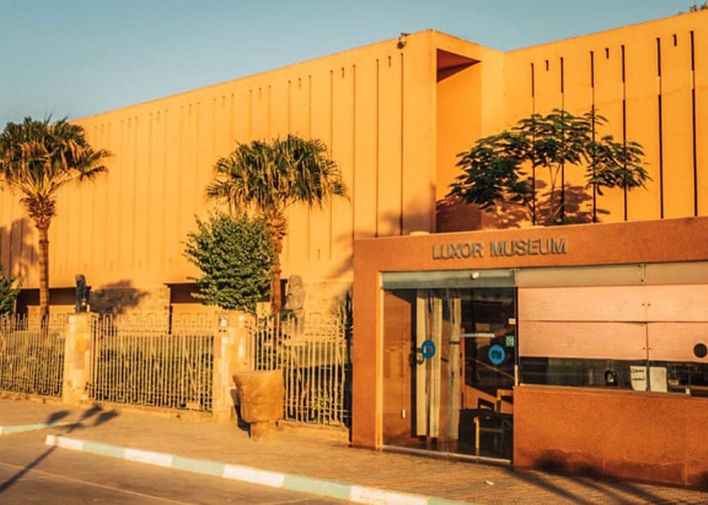 Exterior view of Luxor Museum with its modern, orange facade and surrounding palm trees under clear skies.