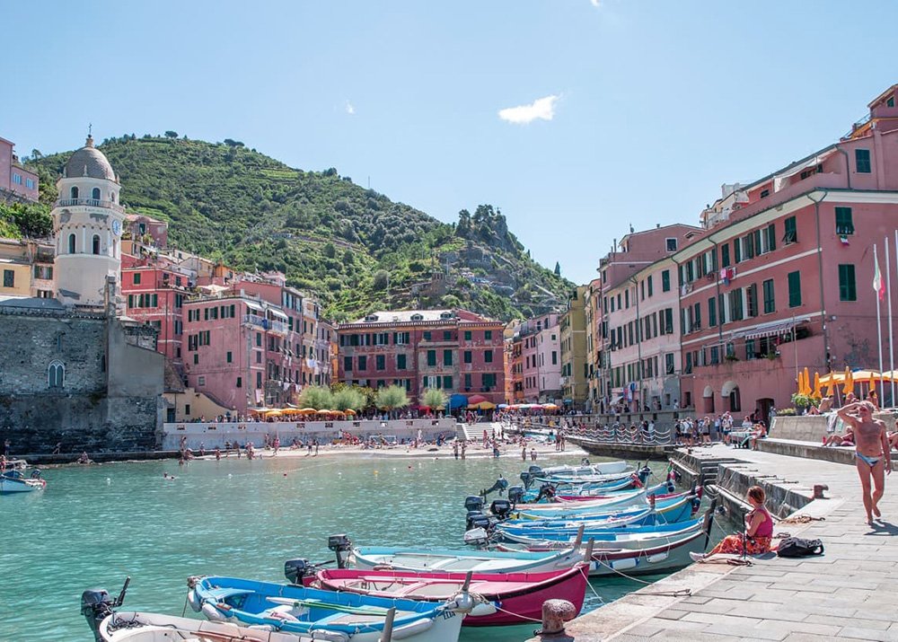 The lively harbor of Vernazza with colorful boats docked and people enjoying the sunny day, showing the bustling and inviting atmosphere of this Cinque Terre village.