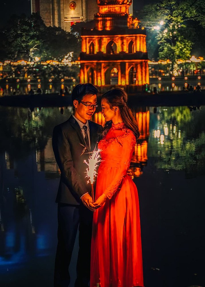 Newlyweds pose at night in front of the Hoan Kiem Lake in Hanoi - Vietnam: A couple posing for wedding photos at night by the lit-up Hoan Kiem Lake.