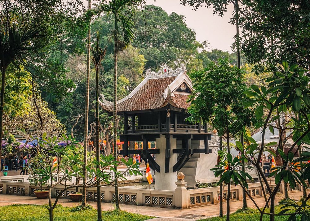 A pagoda standing on one pillar with a brown tiled rood is surrounded by trees and plants.