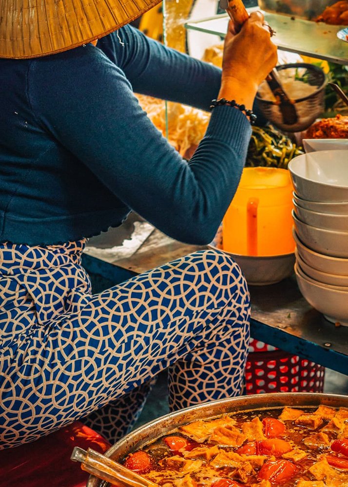A woman making Bun Rieu in Backpacker street in Hanoi, Vietnam: A woman preparing Bun Rieu, a Vietnamese noodle soup, at a street food cart.