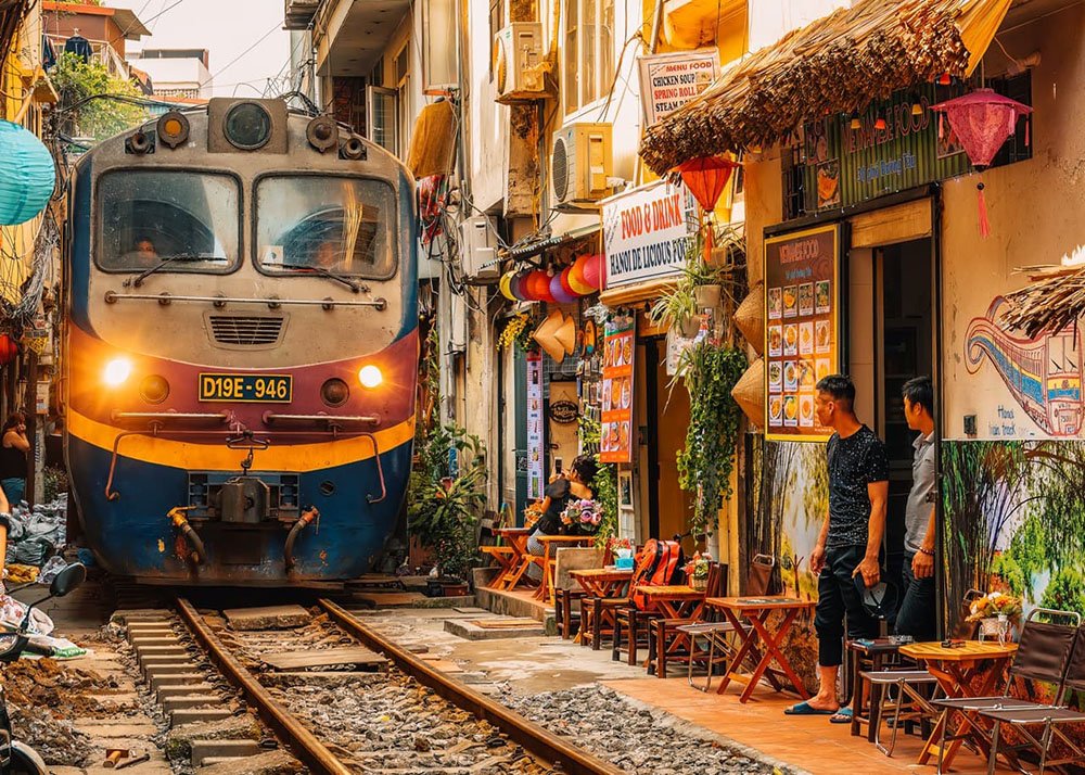 Train passing through train street in Vietnam's Hanoi: A train making its way through the narrow Train Street, with people watching from the sides.