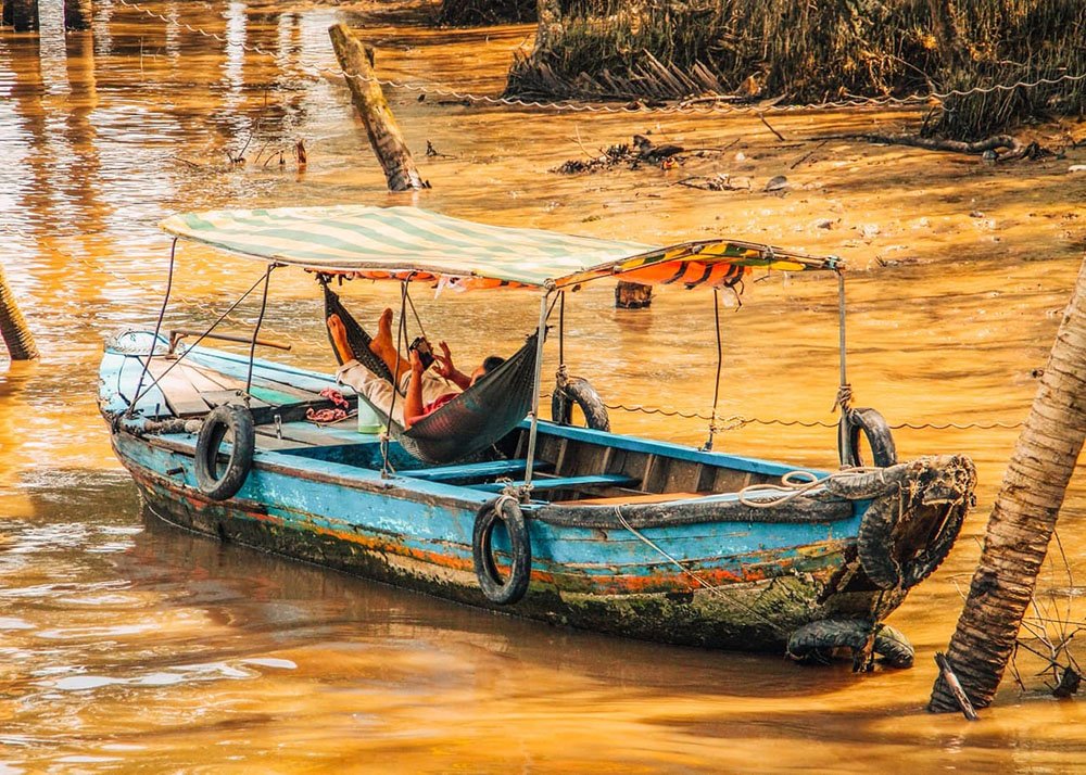 A man is taking a nap in a hammock he attached to two poles inside his partically covered wooden electric boat