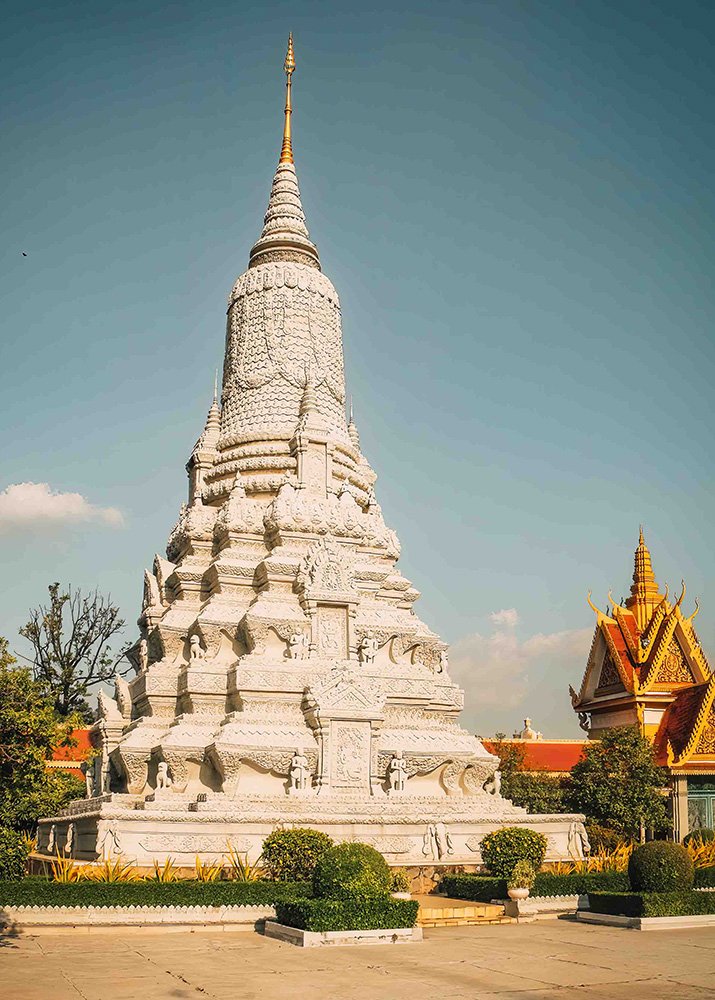 A close-up of a white, intricately carved stupa within the Royal Palace complex in Phnom Penh, Cambodia, on a clear day. The stupa's detailed patterns stand out against the backdrop of traditional Khmer architecture and a clear blue sky.