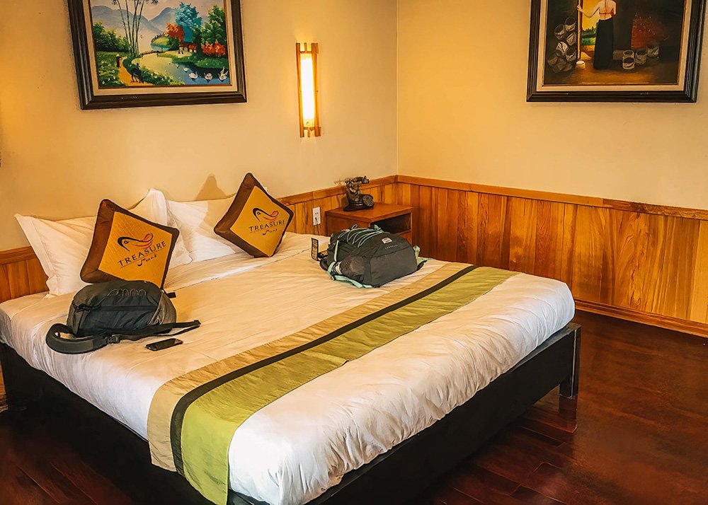 Spacious hotel room with double bed: A hotel room with a large double bed adorned with green and white bedding, two pillows, and paintings on the walls, creating a cozy atmosphere.