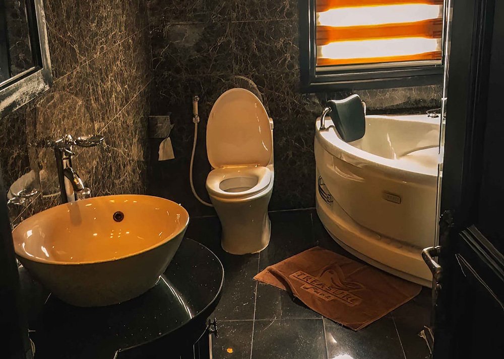 Modern hotel bathroom: A bathroom with a modern design, featuring a round sink, a toilet, and a bathtub, with brown marble walls and a window with blinds.