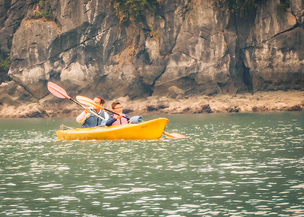 Mother and son kayaking near limestone cliffs in Halong Bay: A father and son paddling a yellow kayak near the limestone cliffs of Halong Bay, enjoying the serene water and scenic views.
