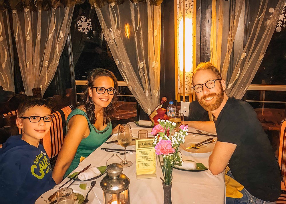 Family dining on a cruise ship: A family of three smiling and enjoying a meal at a beautifully set table inside a cruise ship, with festive decor and a cozy ambiance.