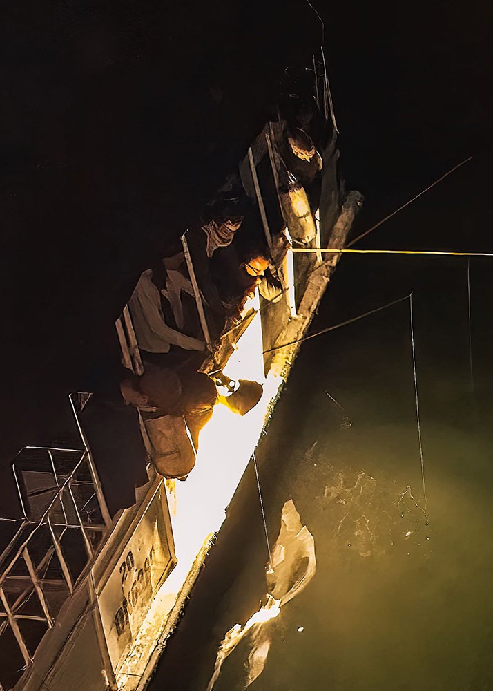 Night fishing from a boat in Halong Bay: People leaning over the side of a boat at night, illuminated by lights, engaging in night fishing in the waters of Halong Bay.