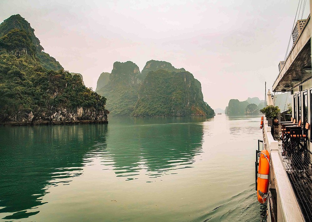 Scenic view of Halong Bay from a boat: A serene view of Halong Bay with calm waters and towering limestone islands, as seen from the side of a boat.