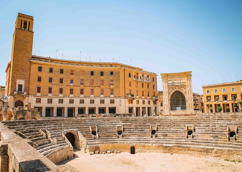 Roman Amphitheater in Lecce: The ancient Roman amphitheater in Lecce, with its grand stone seating and historical significance, set against the backdrop of the city's distinctive architecture, attracting curious visitors.