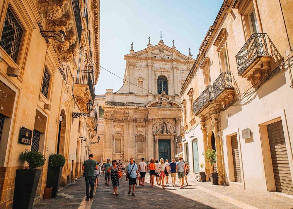 Street in Lecce: A picturesque street in Lecce, featuring historic Baroque architecture with intricate details, where tourists stroll leisurely, soaking in the cultural and architectural beauty.