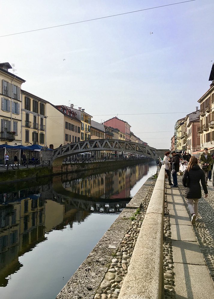Navigli District in Milan: The scenic Navigli district in Milan, featuring a serene canal lined with historic buildings and bustling walkways, perfect for a family stroll and exploration of local shops and cafes.