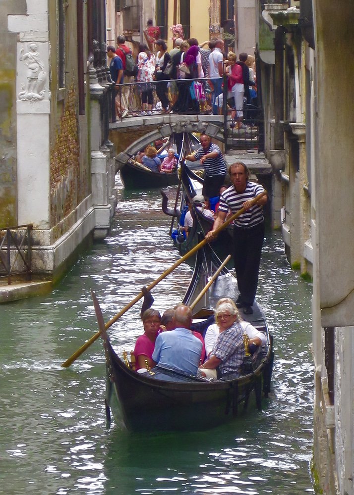Gondola Ride in Venice: A bustling canal in Venice with gondoliers navigating the narrow waterways, filled with tourists enjoying the quintessential Venetian experience amidst historic buildings and charming bridges.