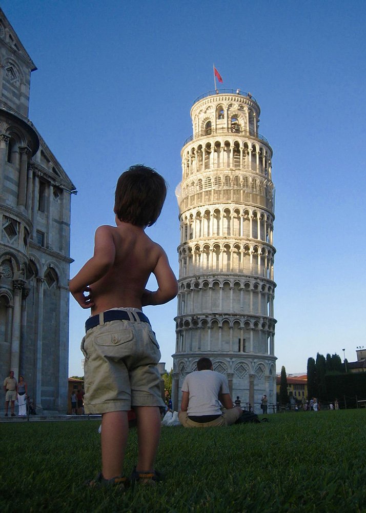 Leaning Tower of Pisa: A young boy in shorts standing in front of the Leaning Tower of Pisa, with his hands on his hips, marveling at the iconic structure, capturing a playful family moment at this famous landmark.