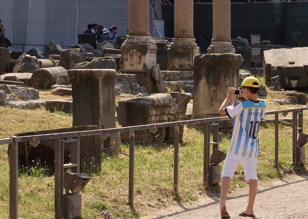 Roman Forum in Rome: A young boy in a Messi jersey taking pictures of the ruins at the Roman Forum in Rome, illustrating a family-friendly exploration of ancient history and architecture.