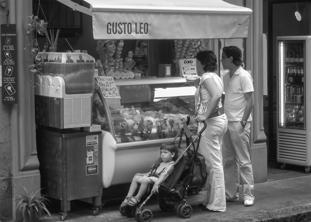 A mother, her brother and toddler in a buggy are ordering gelato in Italy. The picture is a black and white one.