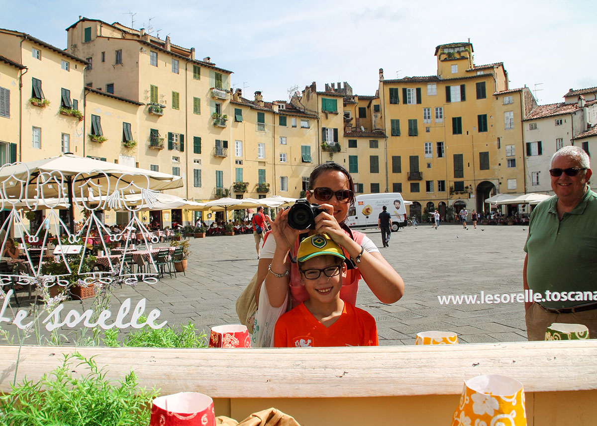 Mom and son take a selfie at Piazza dell'Anfiteatro in Lucca: A lively scene at Piazza dell'Anfiteatro in Lucca, enjoying the outdoor cafes, surrounded by charming historic buildings.