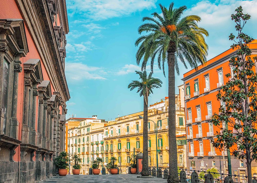 Naples Street Scene: A vibrant street scene in Naples, featuring colorful buildings, palm trees, and a clear blue sky, capturing the lively and picturesque atmosphere of the city.